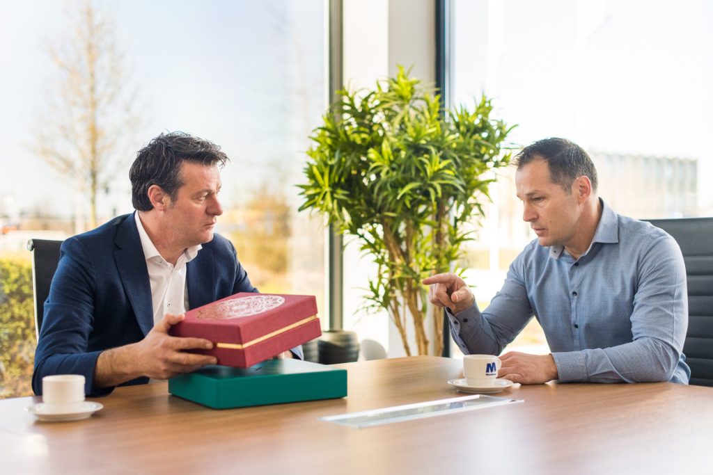 Twee mannen bespreken een doos aan vergadertafel.