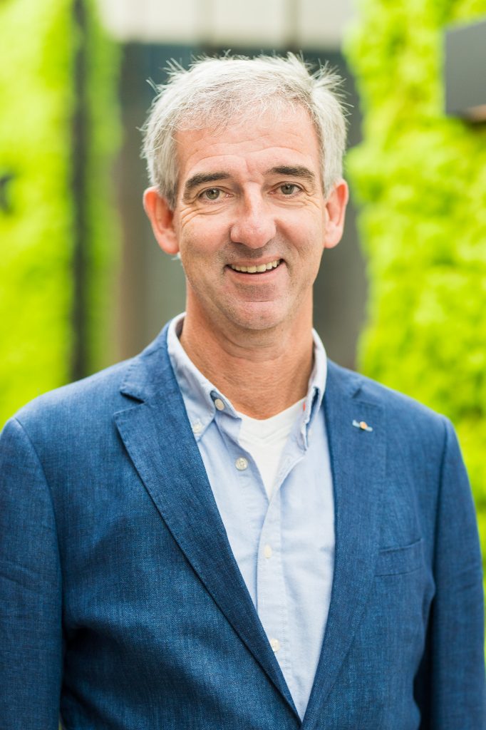 Man in blauwe blazer met groene achtergrond.