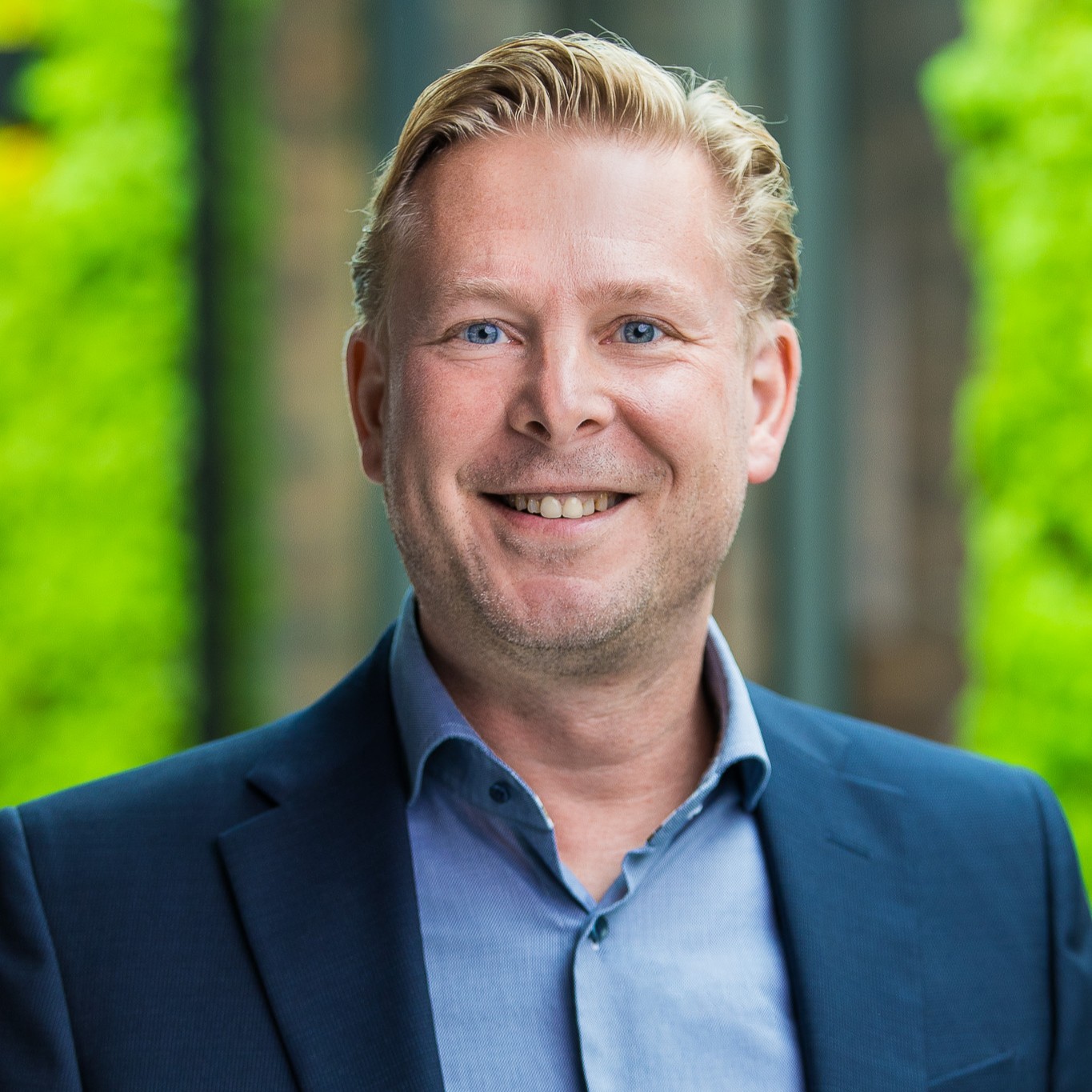 Glimlachende man in blauw pak voor groene achtergrond.