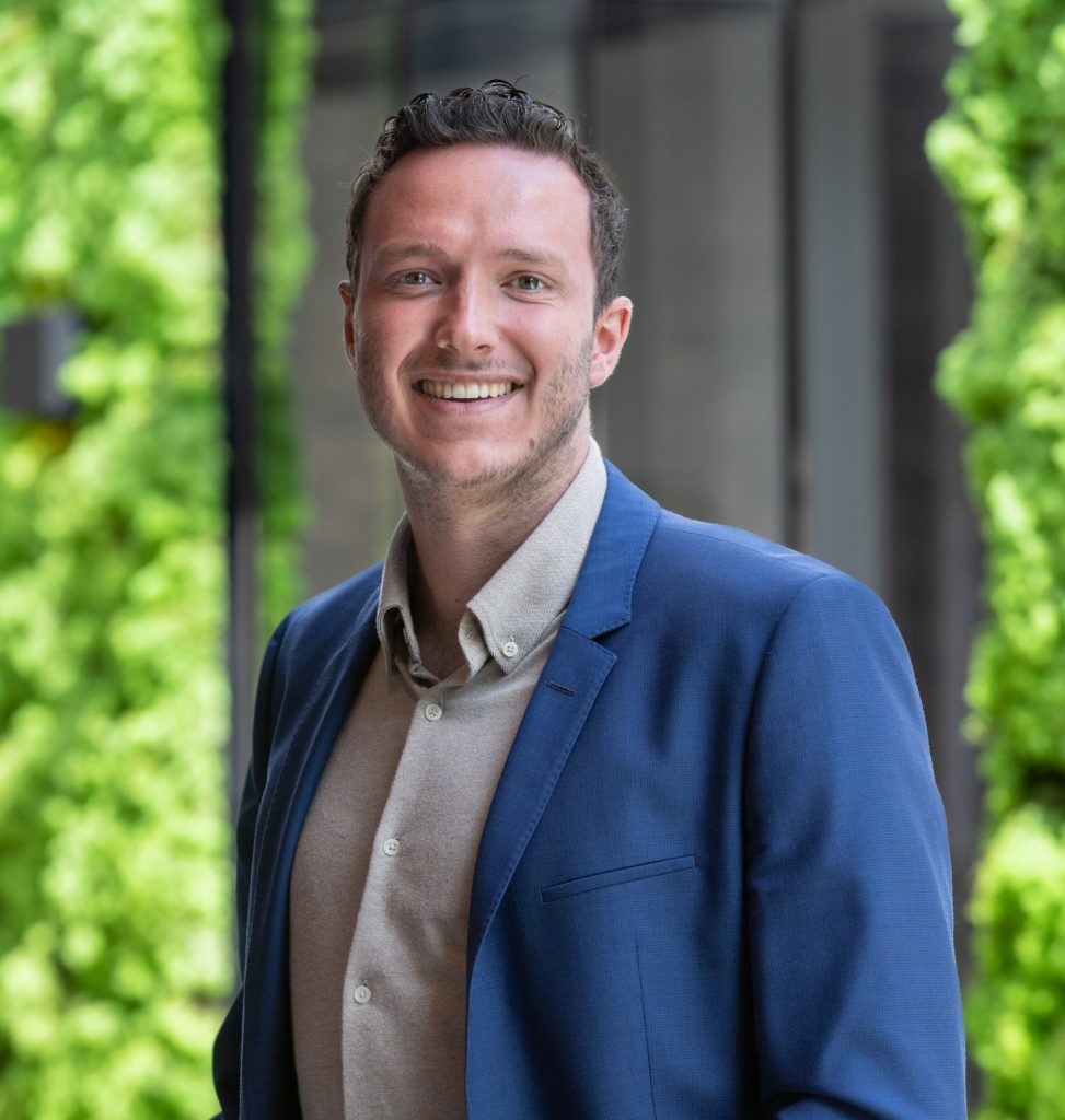 Lachende man in blauw colbert voor groene achtergrond.