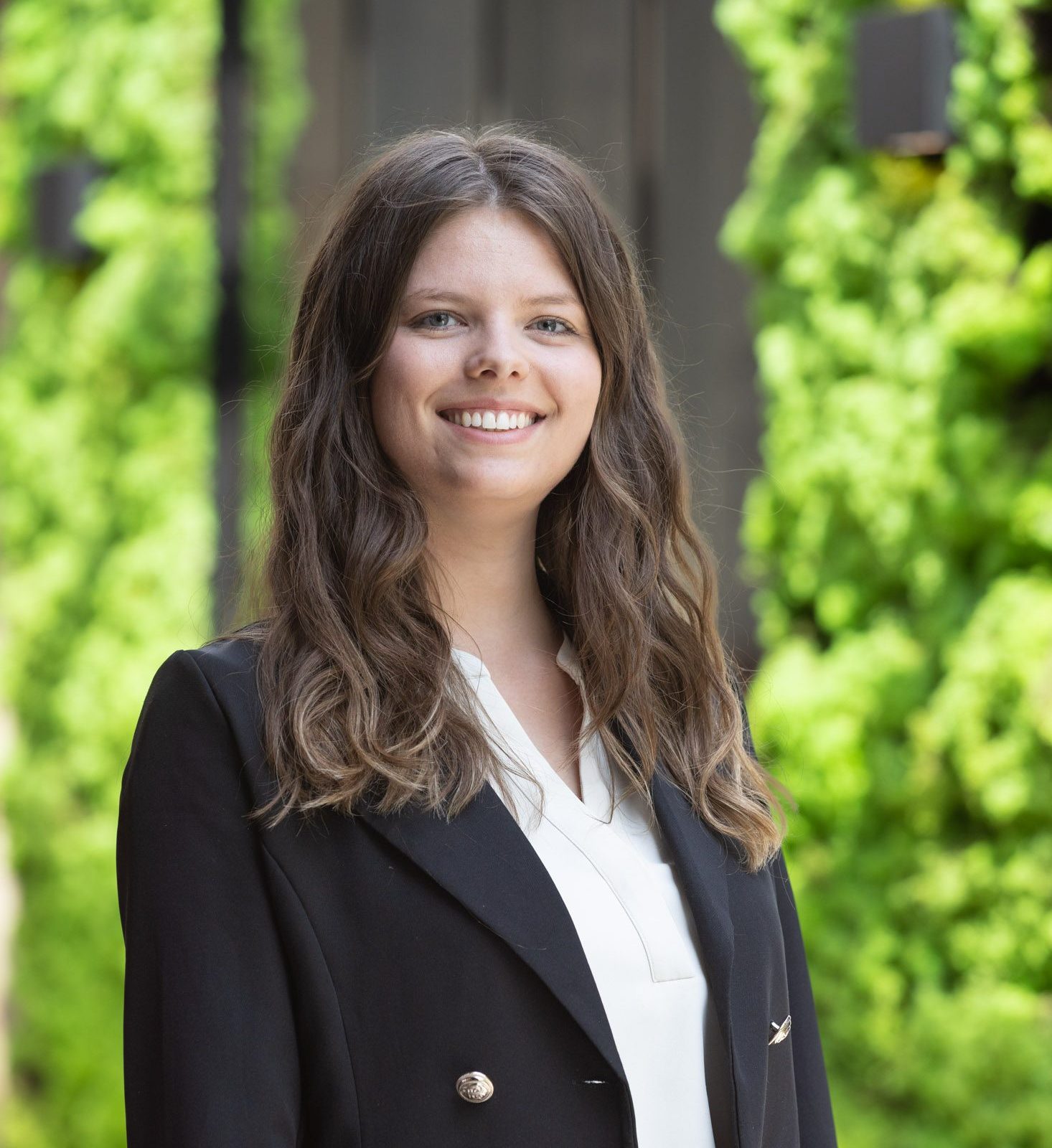 Vrouw in zwarte blazer glimlacht buiten.
