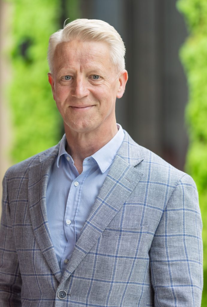 Man in een grijs ruitjespak poseert glimlachend.