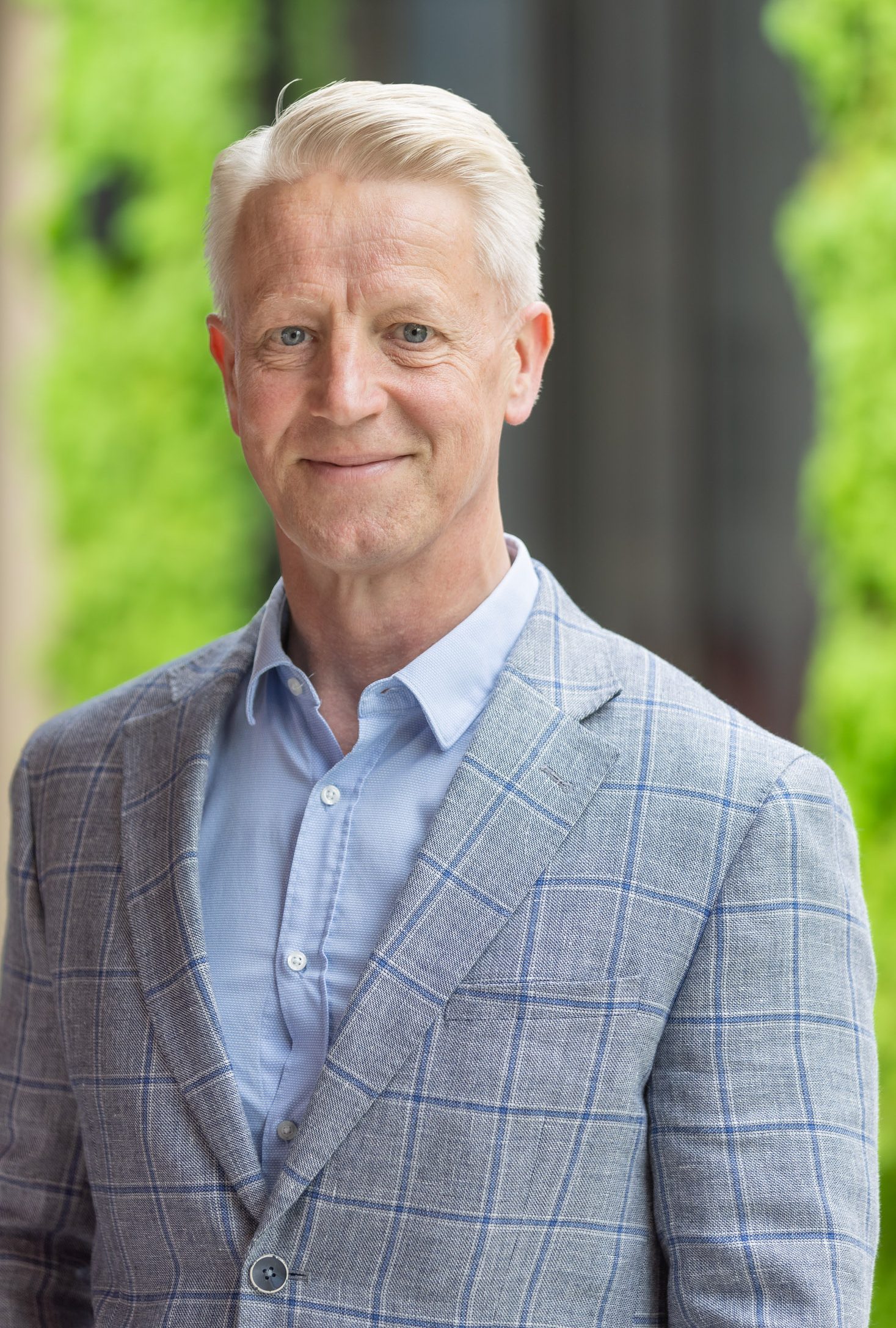 Man in een grijs ruitjespak poseert glimlachend.