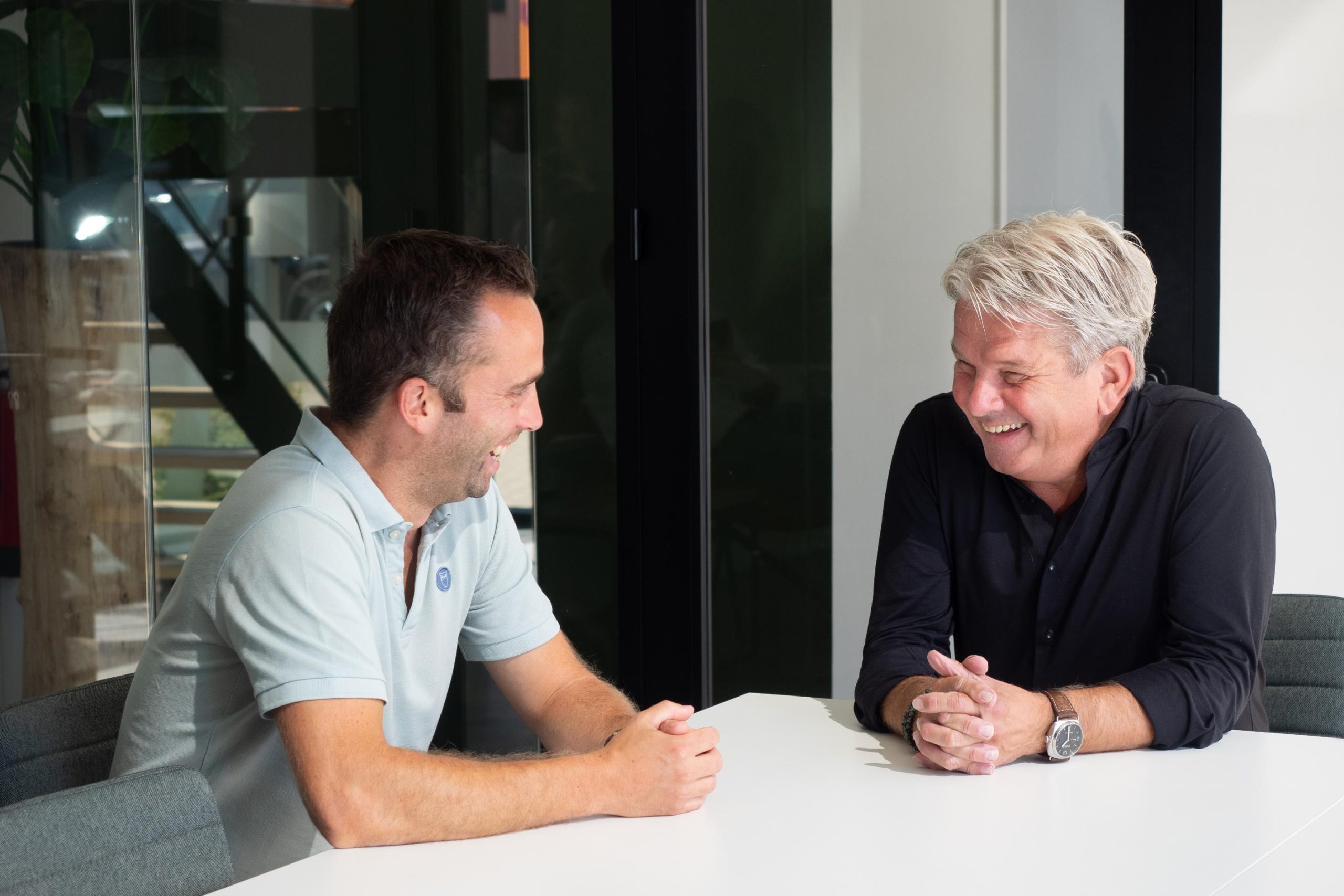 Twee mannen lachen aan een vergadertafel.