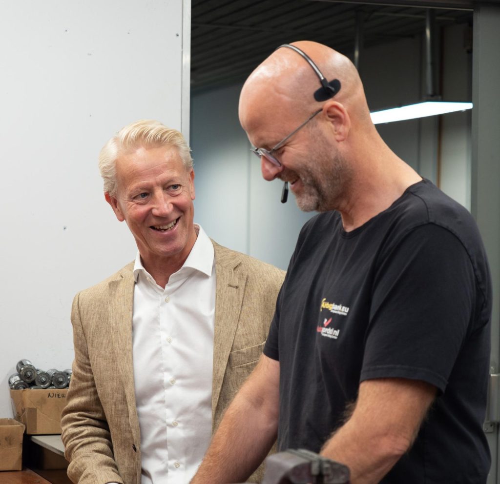 Twee mannen praten lachend in een werkplaats.