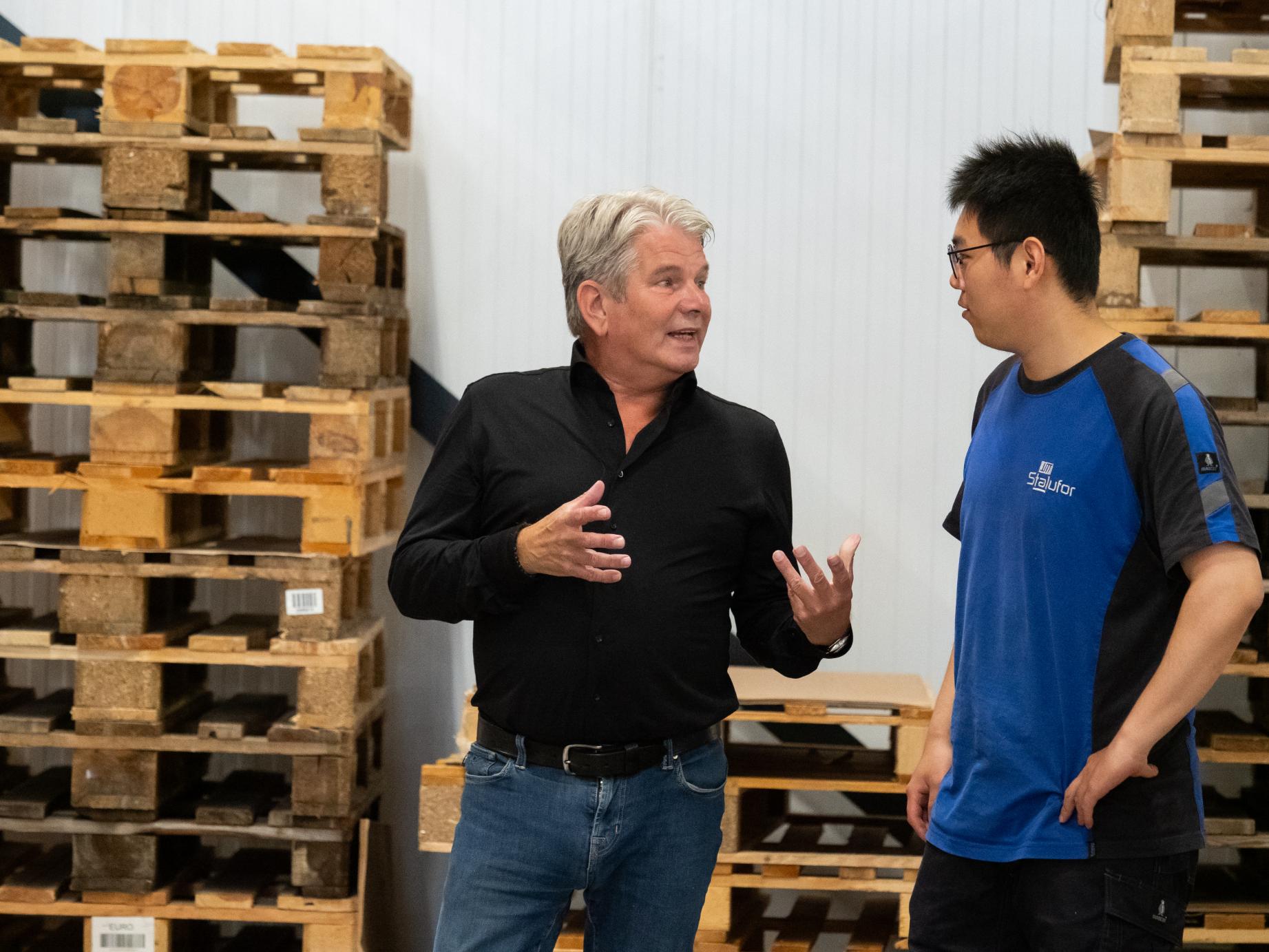 Twee mannen praten in magazijn vol pallets.