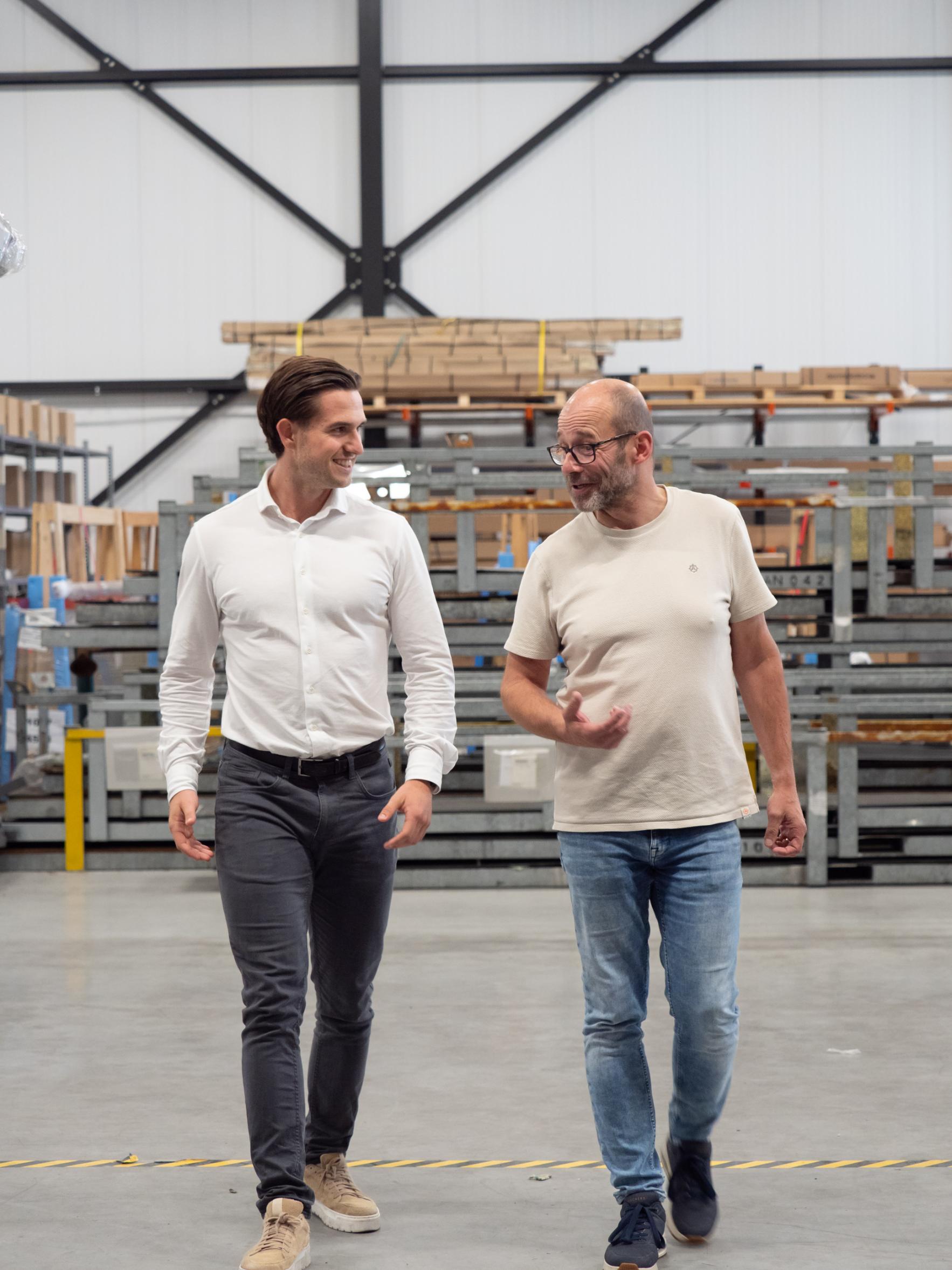Twee mannen lopen pratend in een magazijn.