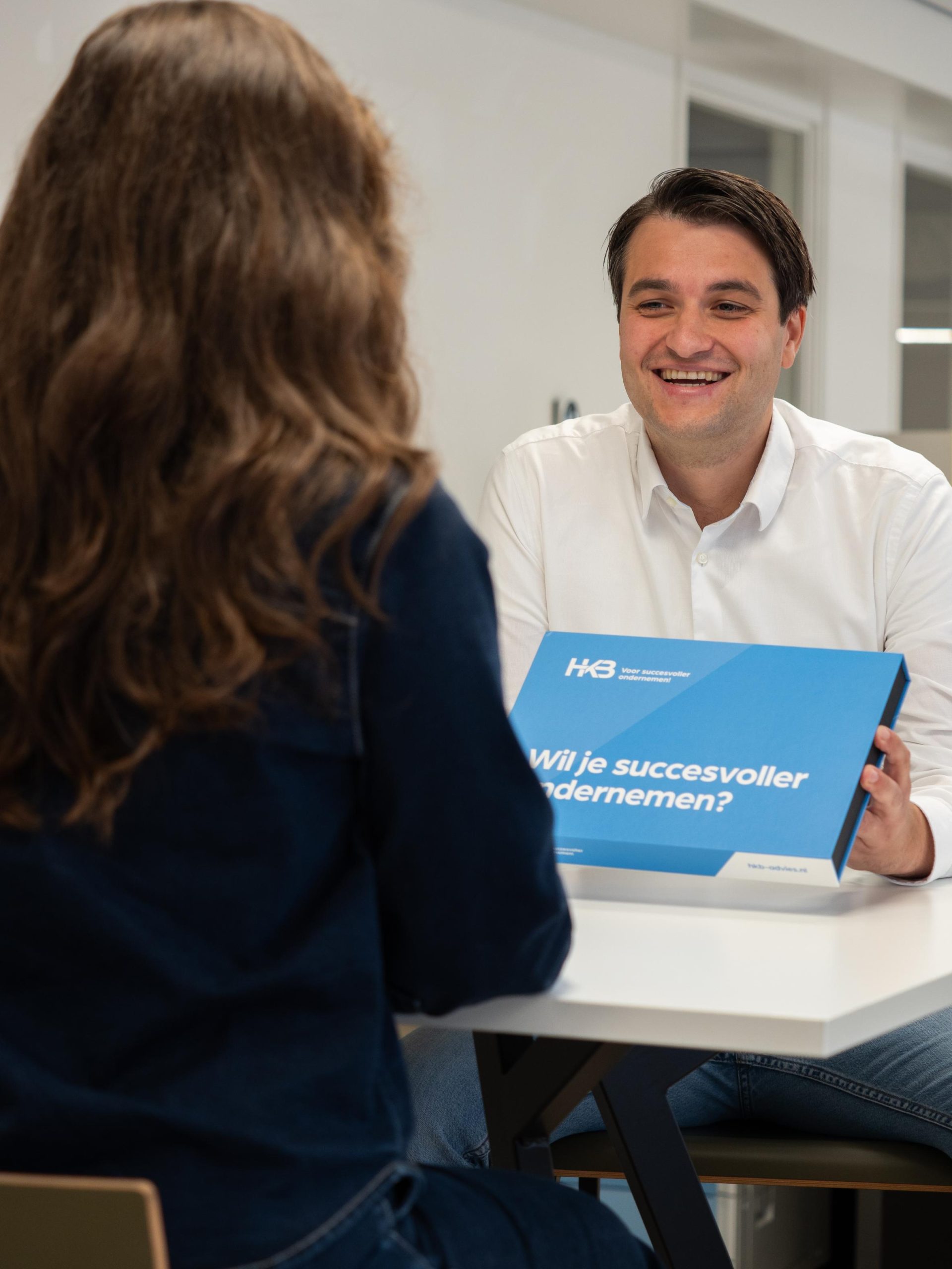 Twee mensen in gesprek met blauwe doos op tafel.