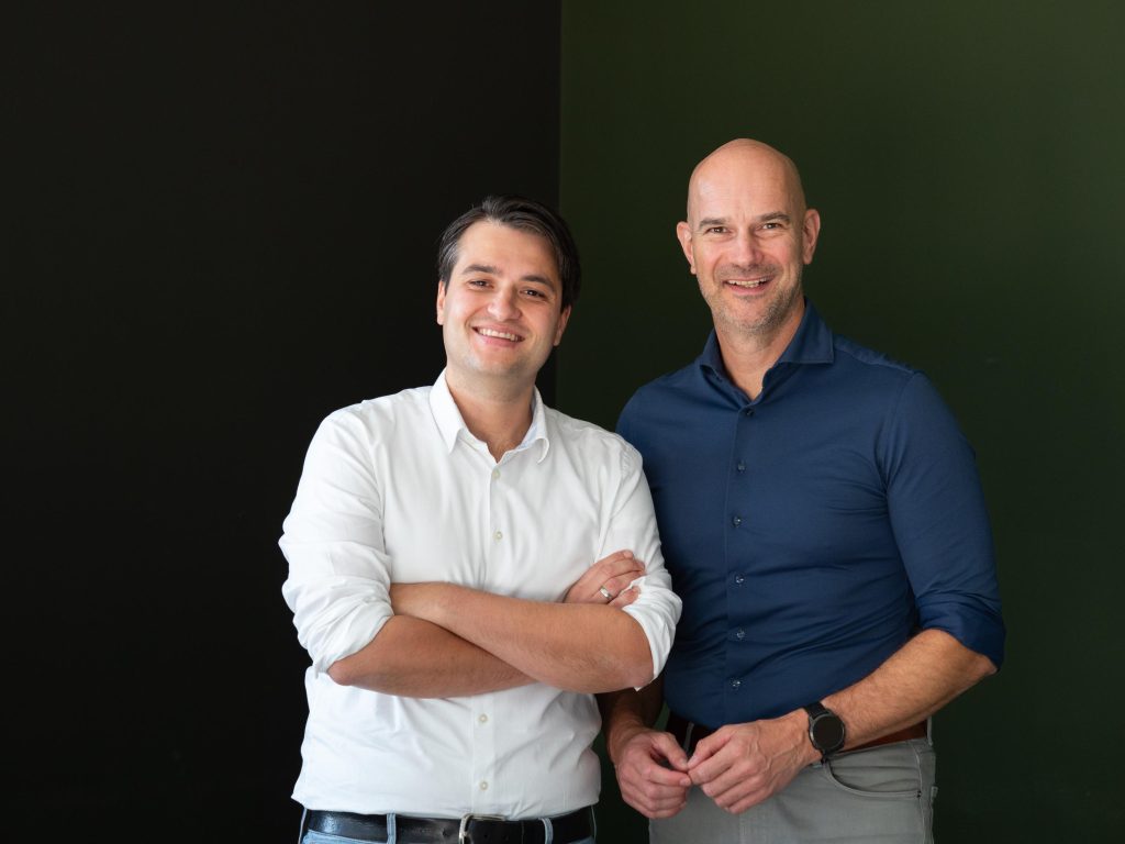 Twee lachende mannen voor zwarte en groene achtergrond.