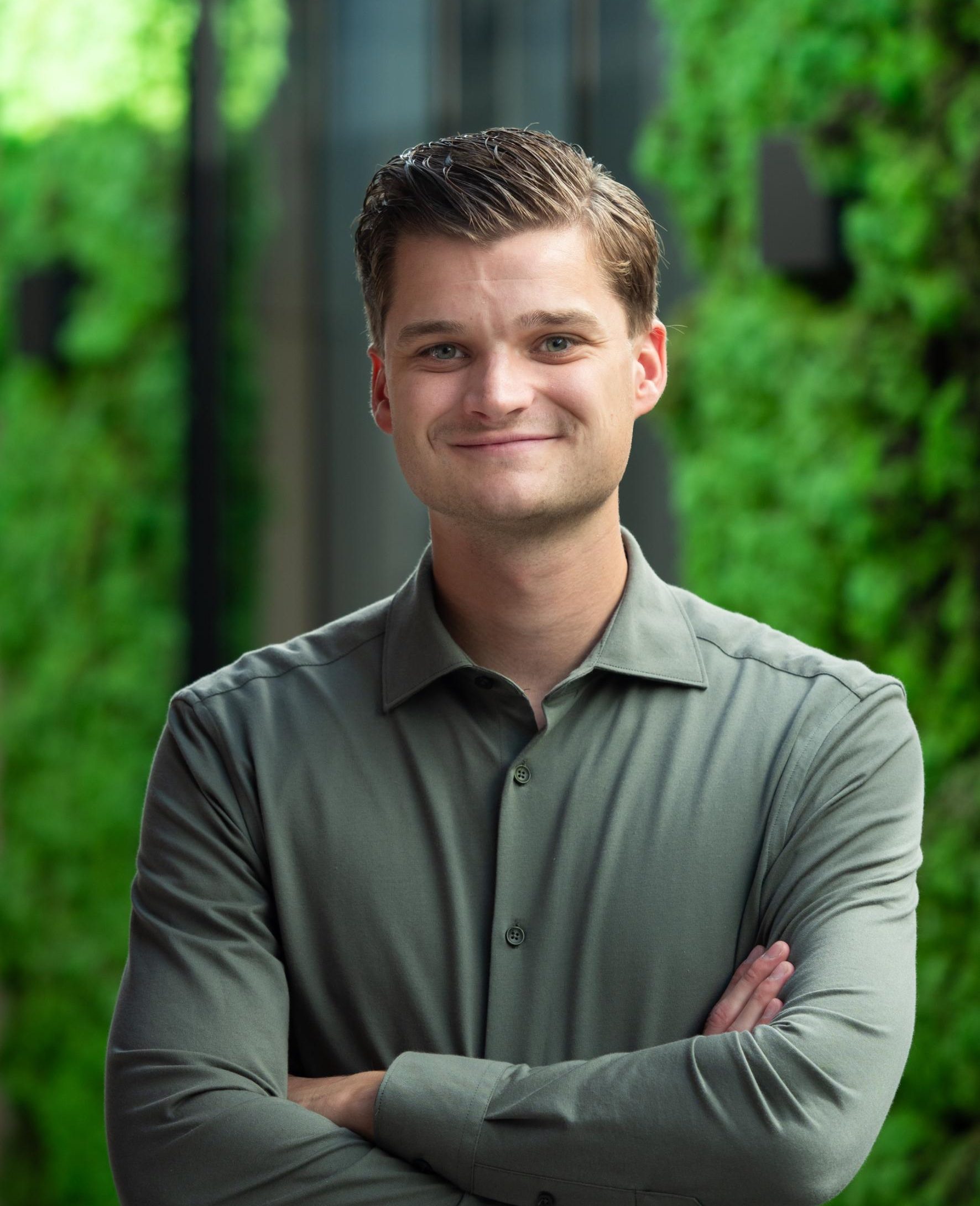 Man met groene blouse, glimlacht naar camera, groene achtergrond.