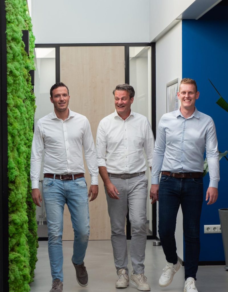 Drie mannen lopen in moderne kantoorhal met groene wand.