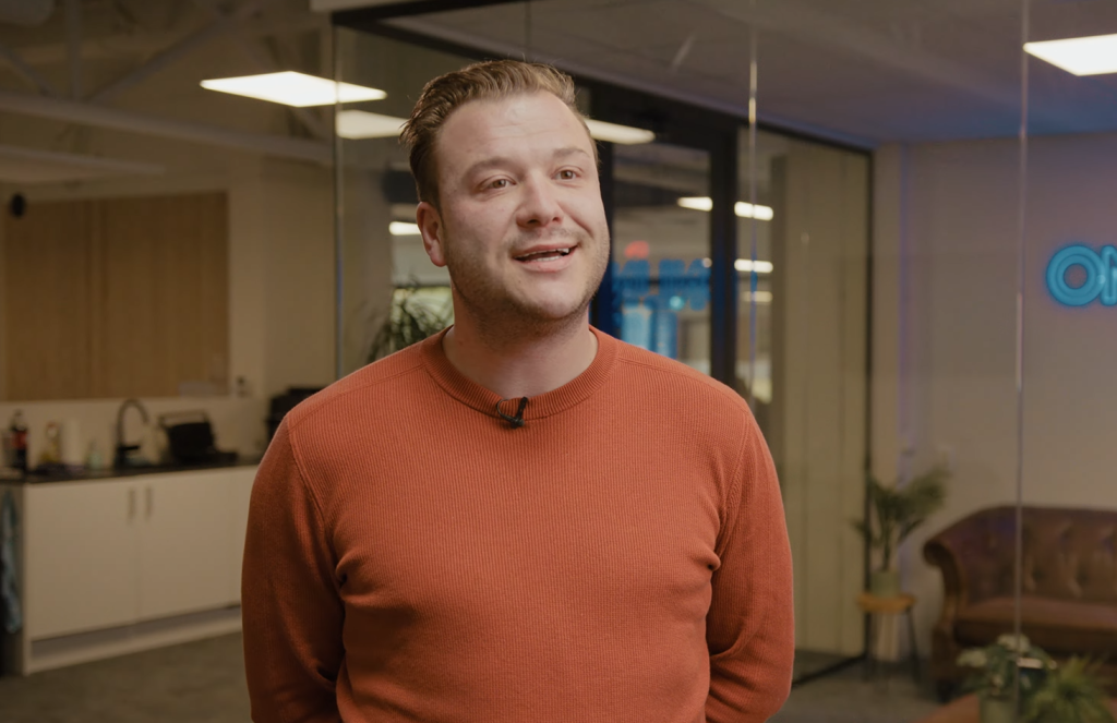 Man in oranje trui in kantooromgeving.