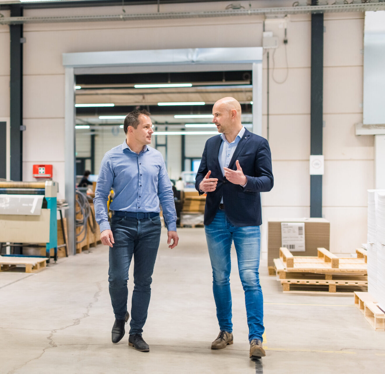 Twee mannen wandelen en praten in een fabriekshal.