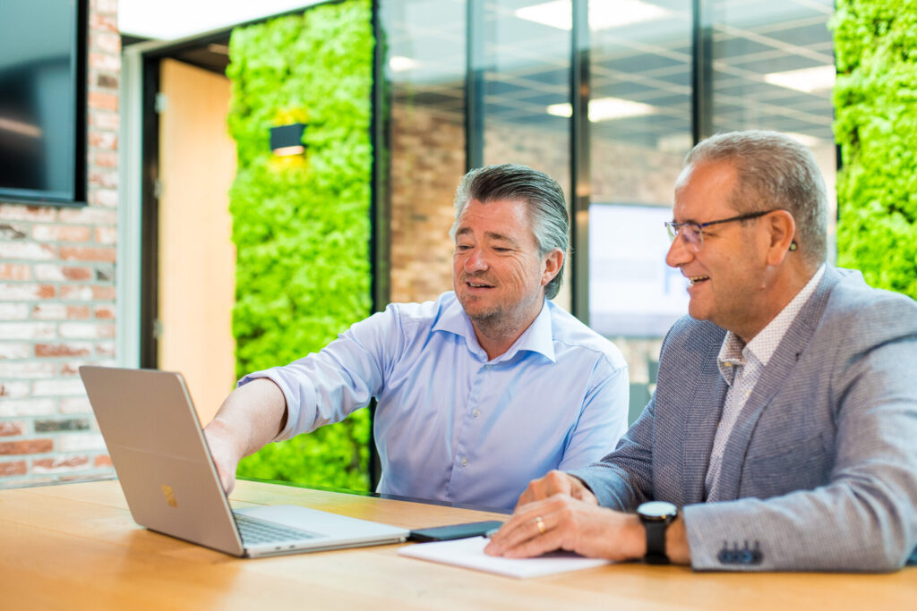 Twee mannen overleggen bij laptop.