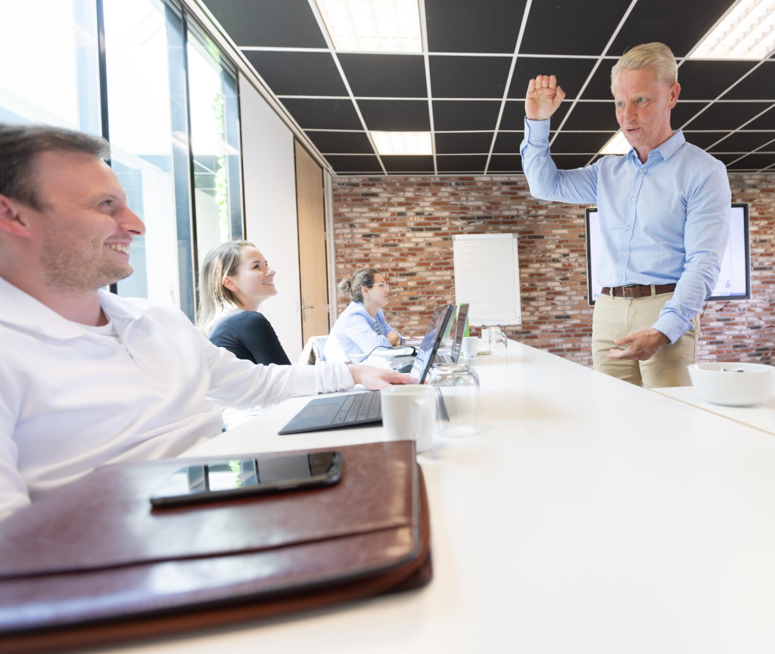 Vergaderruimte met lachende mensen en presentator.