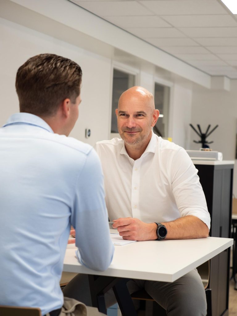 Twee mannen in gesprek aan een tafel op kantoor.