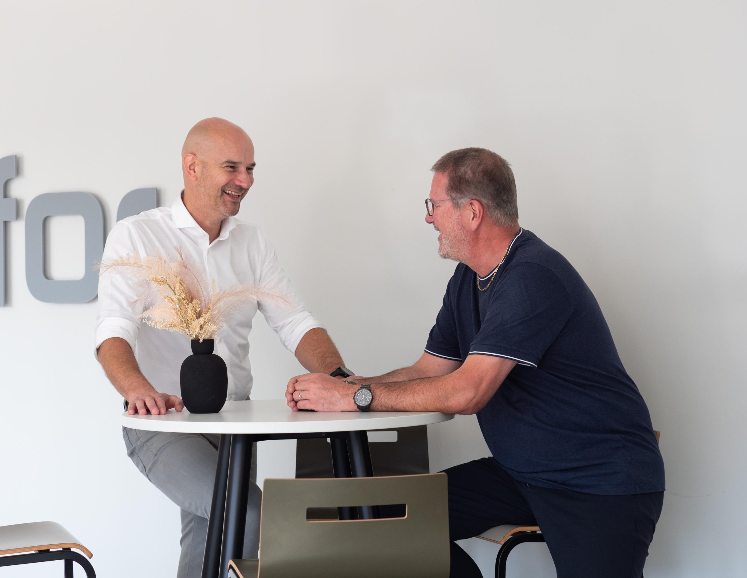 Twee mannen praten aan tafel met een vaas.