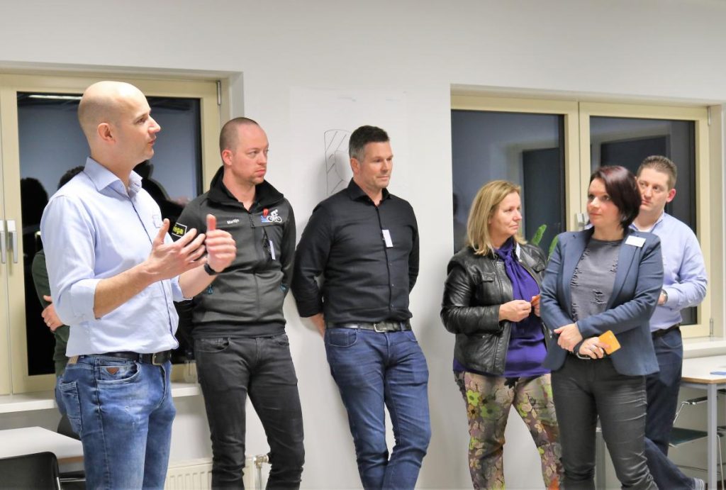 Groep mensen luistert naar presentatie in kantoorruimte.