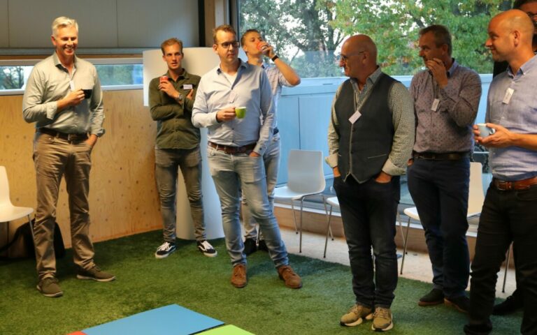 Groepsbijeenkomst in vergaderruimte met zes mannen.