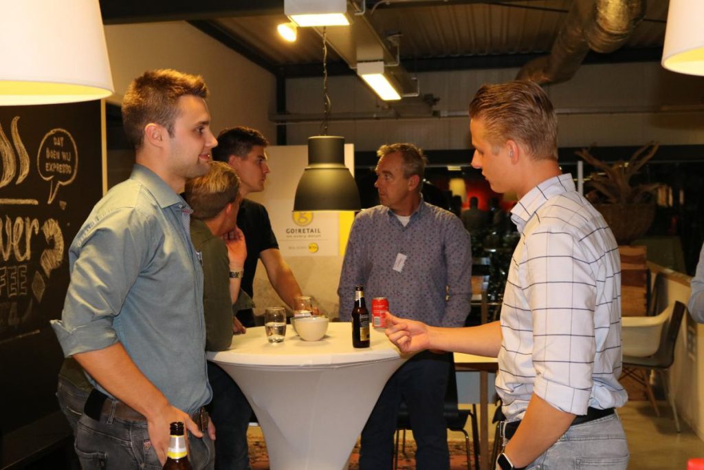 Mensen in gesprek rond hoge tafel met drankjes.