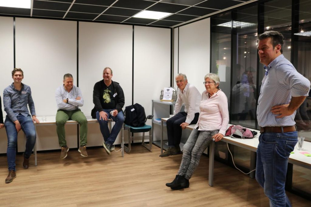 Groep mensen zit en staat in kantooromgeving.