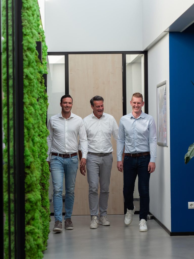 Drie mannen lopen door modern kantoor met groene muur.