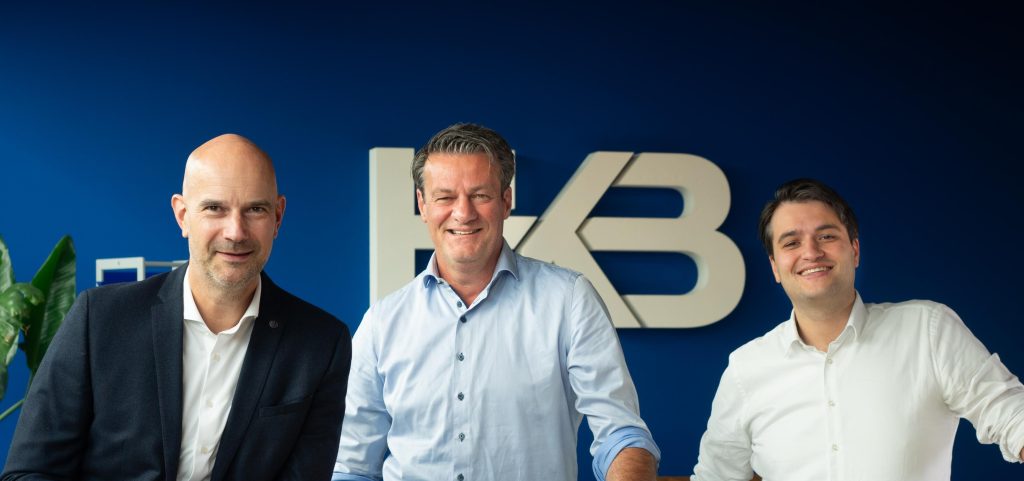 Drie mannen poseren voor een bedrijfslogo.